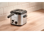 Stainless steel deep fryer on a wooden countertop with white tiles in the background.