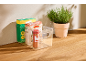 Clear organizer with pasta, spices, and a box, next to a potted herb plant.