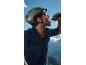 Cyclist in helmet and jersey drinking from a water bottle, with mountains in the background.
