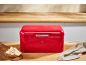 Glossy red bread bin on a wooden countertop with a sandwich and a cloth.