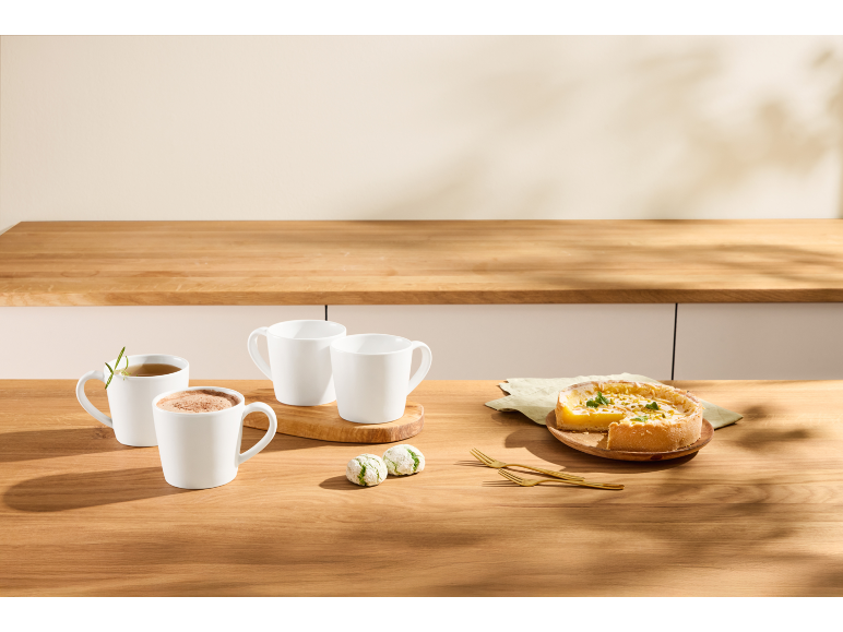 White mugs with hot drinks, cookies, and a lemon tart on a wooden table.