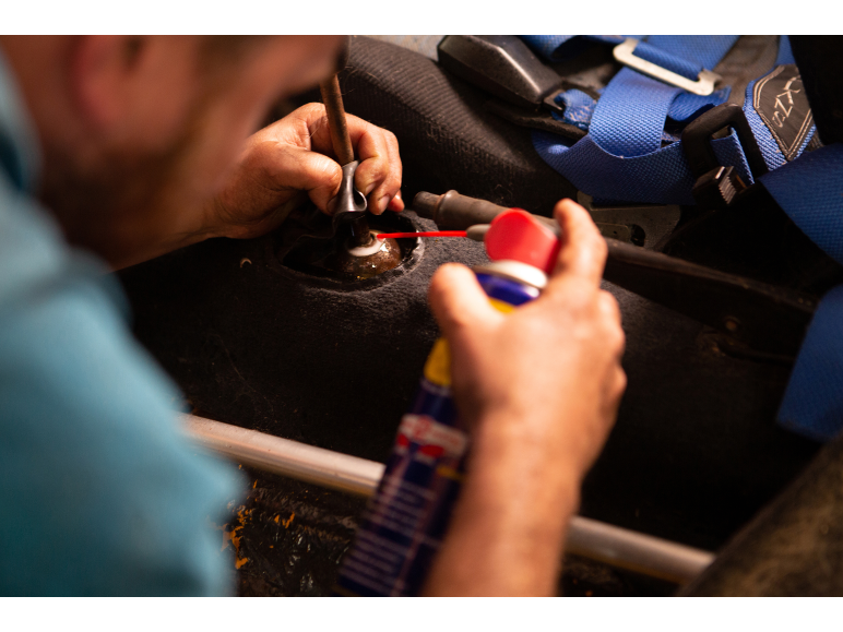Man applying spray lubricant to a car gear stick.