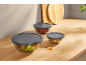 Glass bowls with gray lids, containing salad, berries, and walnuts, on a wooden table.