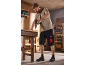 Man in work t-shirt and shorts drilling a board in a workshop.