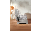A silver food slicer with a clear plastic tray on a wooden countertop.