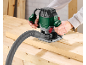 Person using an electric router with a vacuum hose on a wooden workbench.