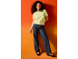 Woman in a light green t-shirt and dark blue jeans, posing against an orange background.