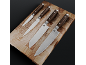 Four kitchen knives with wooden handles and patterned blades on a wooden cutting board.