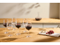 Red wine glasses, some filled, with a decanter, cheese, and grapes on a wooden table.