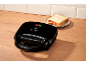 Black sandwich maker on a wooden countertop with slices of bread on a plate.
