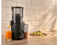 Black juicer making fresh orange juice with fruit on cutting board.