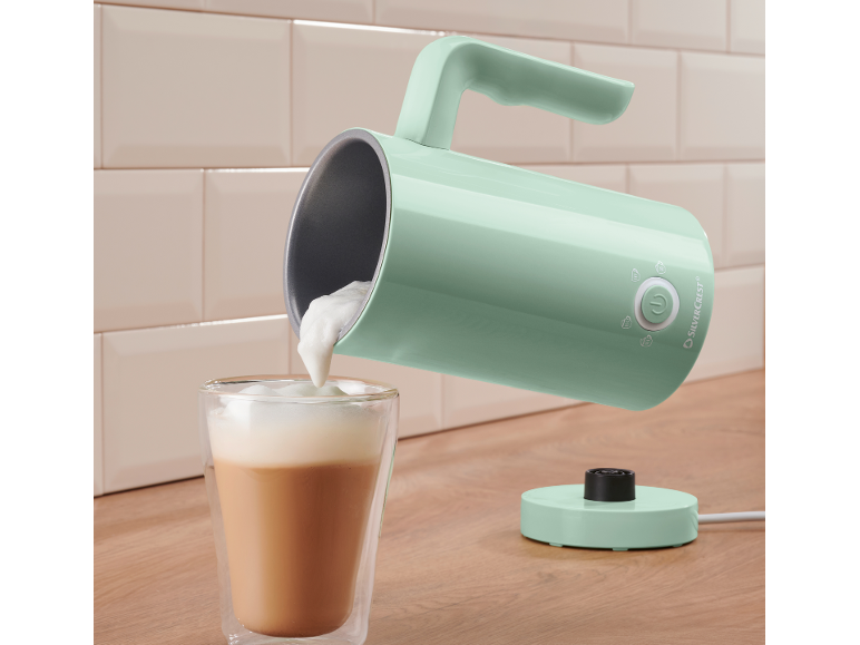 Mint-colored milk frother pouring foam into a glass of coffee.