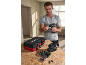 Man holding a cordless drill, with a tool case, battery charger, and bit set on a wooden table.