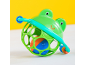 Green frog-shaped baby rattle with a colorful ball inside, on a white and yellow background.