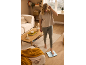 Woman weighing herself on a scale in a cozy living room.