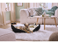 Dog in a dog bed on a fluffy rug in a living room with a sofa and coffee table.