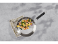 Stainless steel pan with chicken, gnocchi, spinach, and red onion on a grey background.