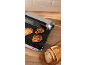 Electric grill with two steaks and a slice of toasted bread, sliced bread on a board.