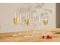 Seven champagne flutes, three filled with sparkling wine, and three raspberries on a wooden table.