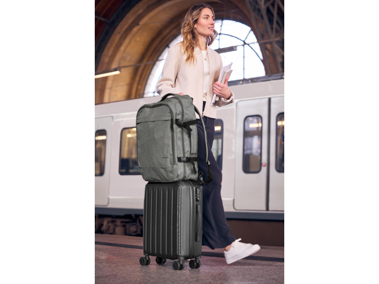 Woman with a backpack and a wheeled suitcase at a train station.