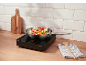 Portable cooking hob with a pan of vegetables, a cutting board, and a kitchen towel.