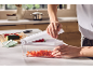 Person using a vegetable chopper to dice red bell peppers in a bright kitchen.