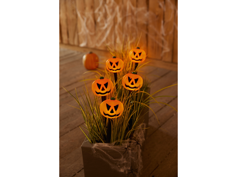 Glowing pumpkin lights in a planter with grass, decorated with cobwebs and spiders.