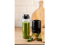 Smoothie blender with a green smoothie, kiwis, and kale on a wooden table.