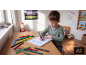 Child writing ABC12 with felt-tip pens at a wooden table in a bright room.