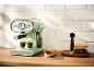 Light green espresso machine with coffee cups, biscuits, and coffee beans on a countertop.