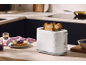 White toaster with toast on a kitchen counter, next to a plate with jam and fruit.
