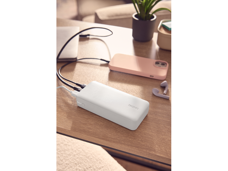 White power bank charging a pink smartphone and a laptop on a wooden table.