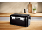 Black bread bin on a wooden kitchen counter with salt and pepper grinders and a plant.