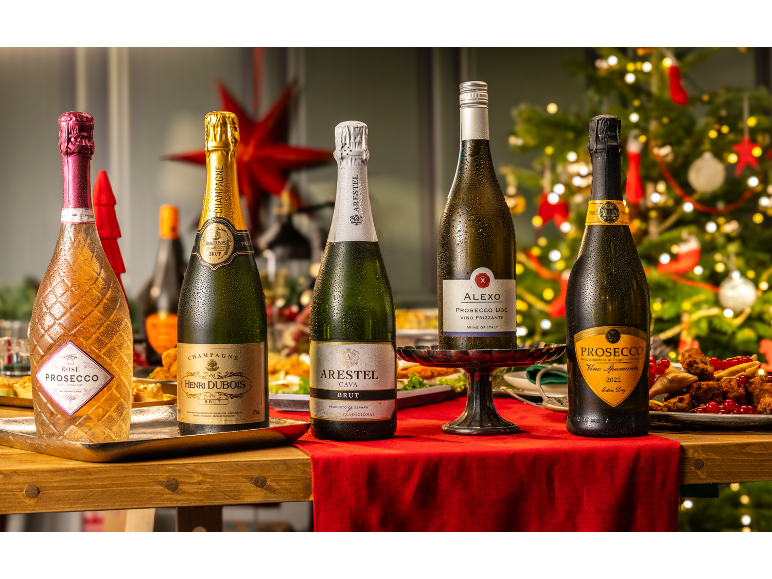 Five bottles of sparkling wine, champagne, and prosecco on a Christmas table with festive decor.