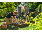 Man and woman planting in a raised garden bed, using gardening tools and gloves.