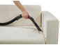 Handheld vacuum cleaner cleaning dirt from a cream sofa.