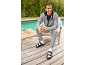 Man in grey tracksuit and black sandals with white socks, smiling while holding a green smoothie.