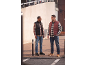 Two men in plaid shirts, puffer vests, jeans, and casual shoes, smiling outdoors.
