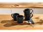 Set of black mugs on a wooden countertop with cookies and sugar sticks.