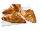 Three golden, crispy croissants on a white cloth.