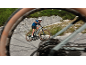 Man cycling on an electric mountain bike on a winding road, viewed through a blurred wheel.
