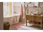 Bathroom with a white bathtub, wooden vanity, pink rug, and towels.