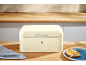 Cream-colored bread bin on a wooden counter with toast and a kitchen towel.
