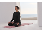 Woman meditating on a yoga mat, with the sea in the background.