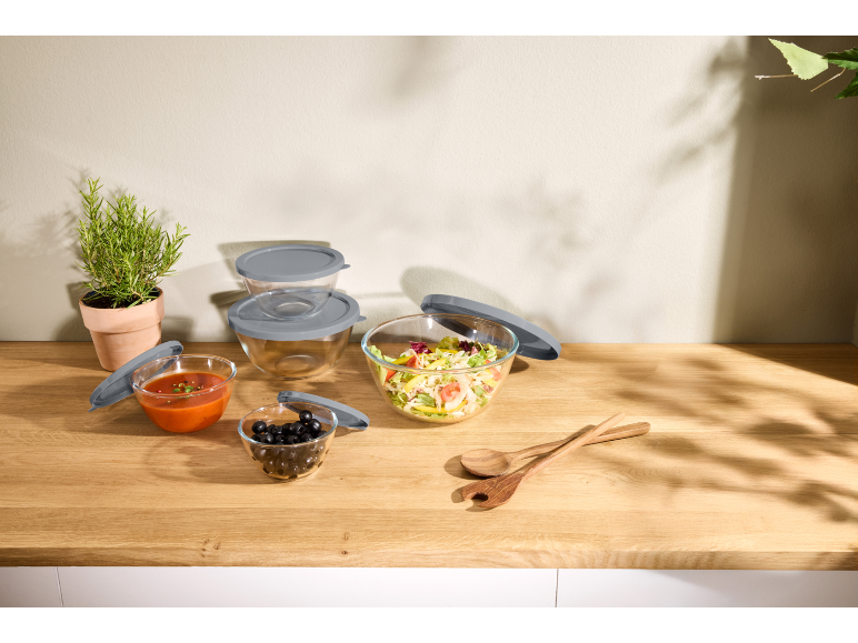 Glass food storage containers with grey lids, filled with salad, sauce, and olives.