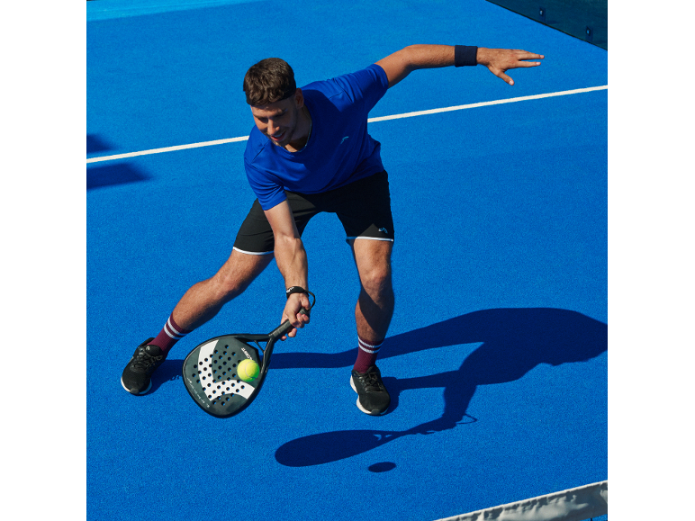 Man in sportswear playing padel on a blue court.