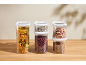 Transparent food containers with pasta, beans, rice, muesli, and lentils on a wooden table.