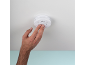 Hand pressing the test button on a ceiling-mounted smoke detector.