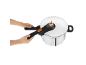 Hands operating a white pressure cooker with black and orange handles.