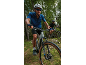 Two cyclists in helmets and sportswear ride mountain bikes on a forest trail.